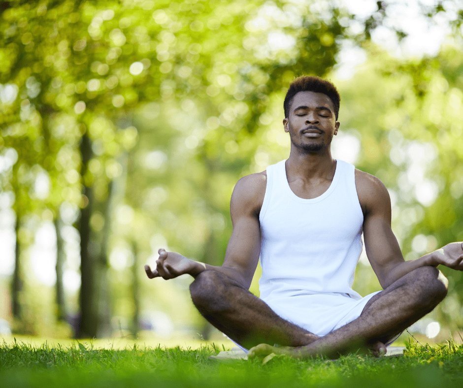 A person with dark skin wearing a white shirt and white shorts meditates 