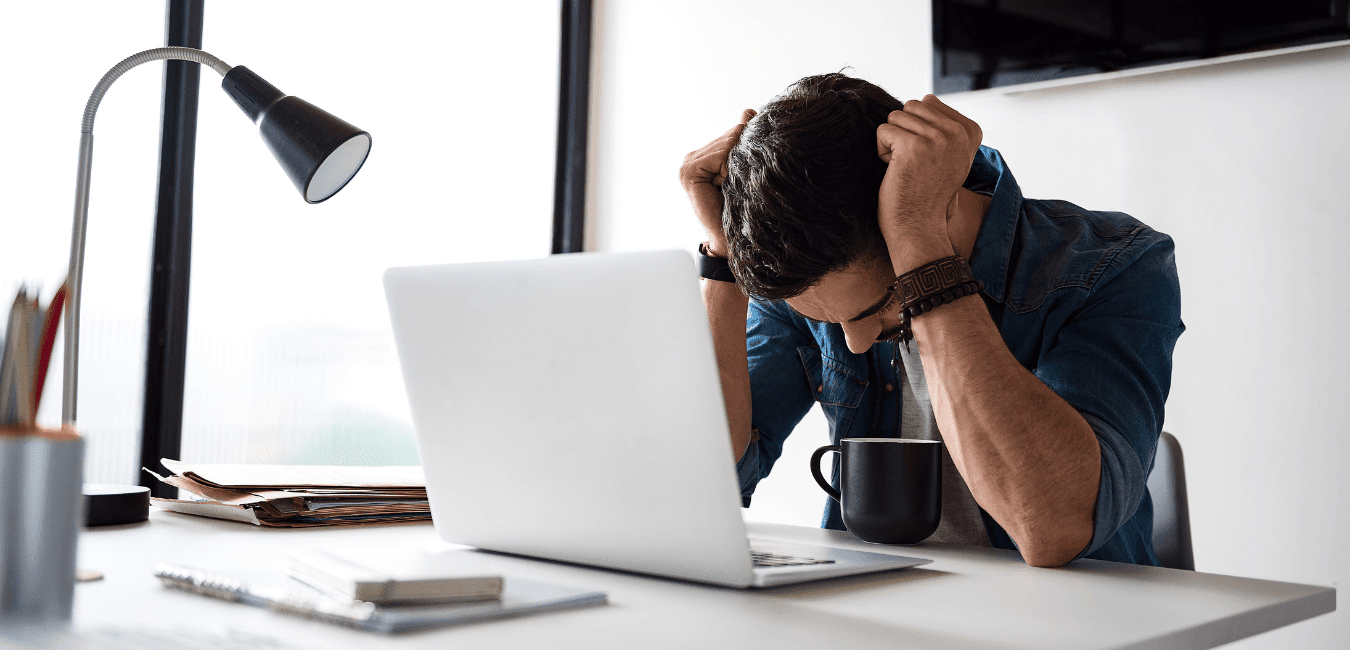 Man sitting on his desk with his hand on his head looking down