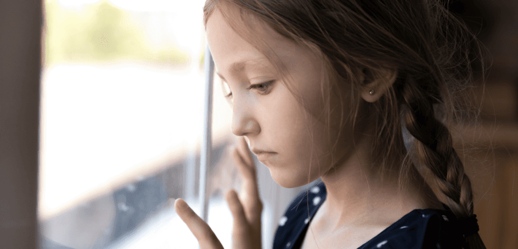 Young girl looks sadly out side the window