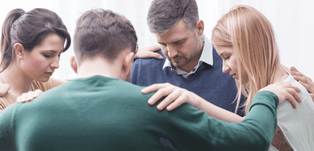Christian people holding each others elbow bowing head in a room for group therapy session