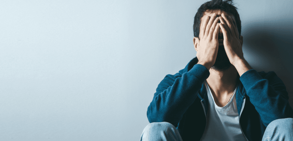 Man sitting on the floor with hand on his face looking depressed