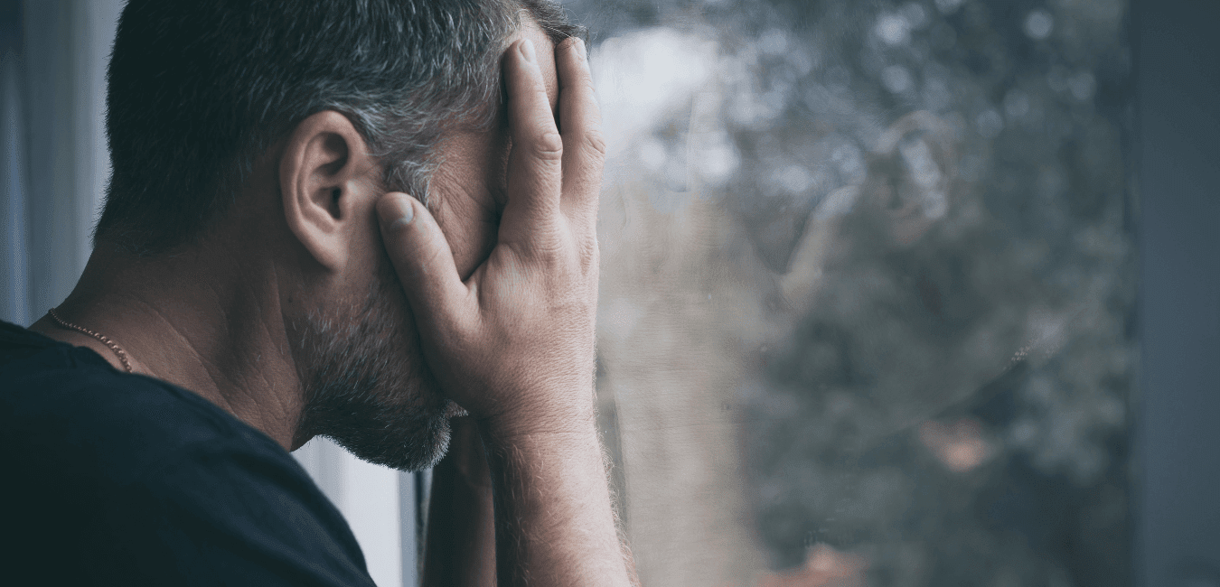 Man looking unhappy facing window with his hand on face sobbing at home