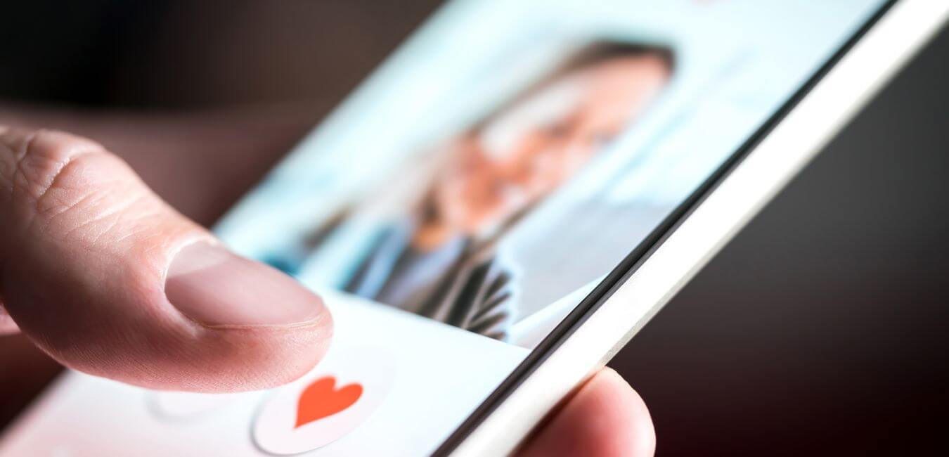 Close-up of a man's hands using a smartphone, tapping 'like' on dating app profiles.