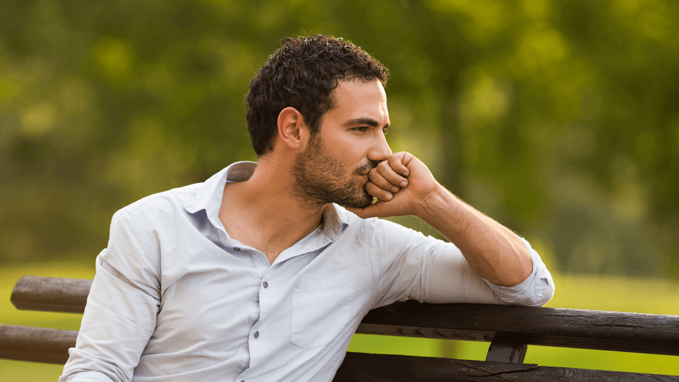 A man reflects in silence while sitting on a wooden bench outdoors