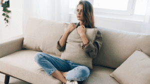 Woman sitting on couch at home, looking sad and holding a pillow