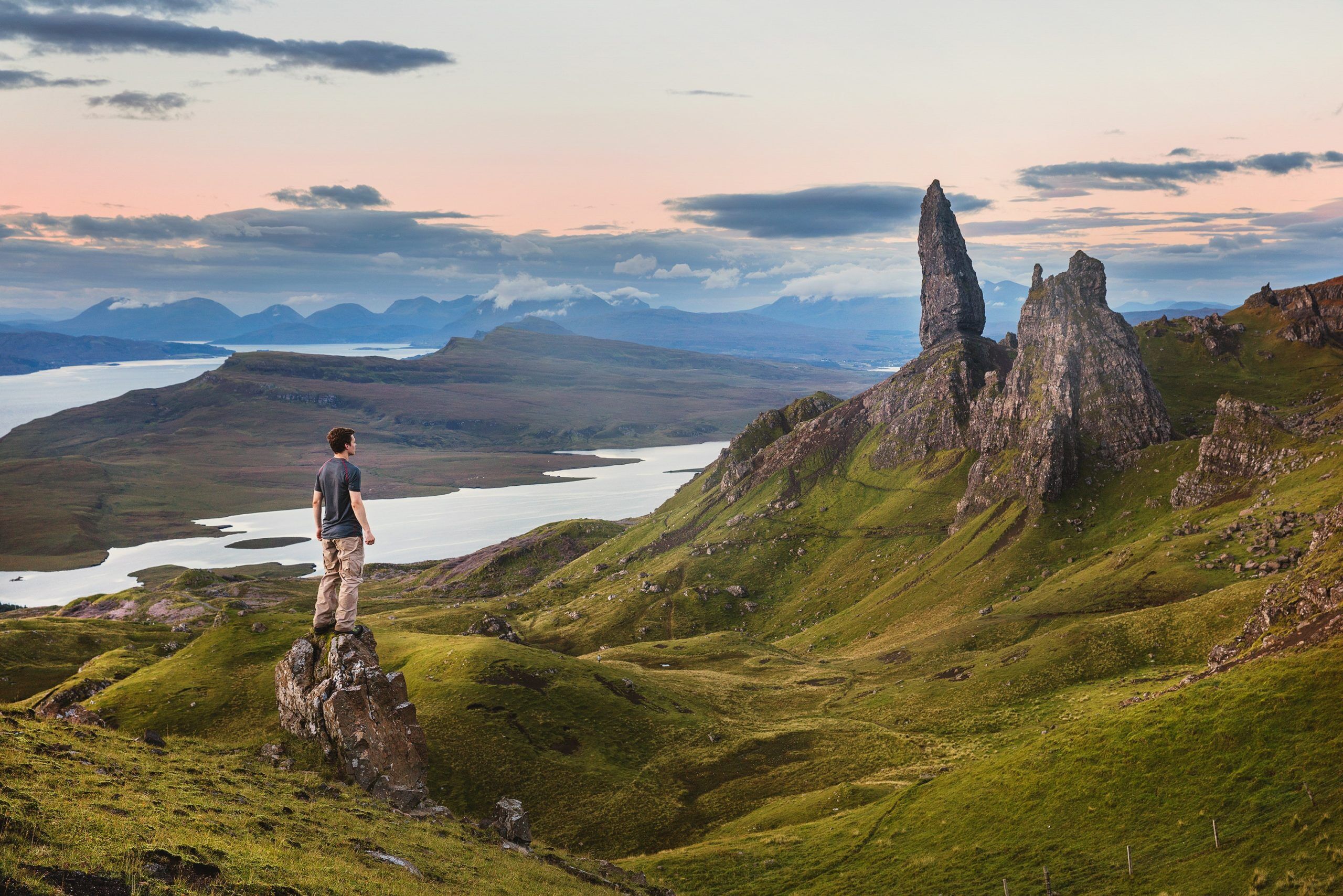 man standing on a rock formation by mountains and water