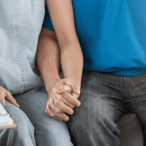 Couple sitting on couch holding hands talking to a therapist writing notes