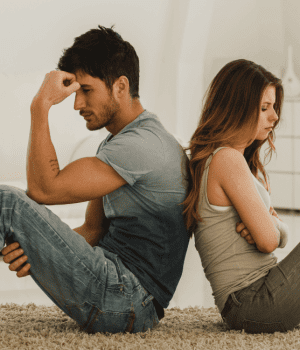 Couple having a problem sitting on the floor back to back in living room