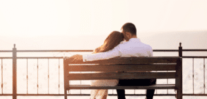 Young married couple sitting affectionately on the beach, watching the sunset.