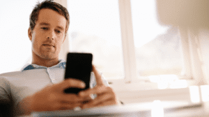 Man sitting and using his phone, with a serious expression while engaged in conversation.