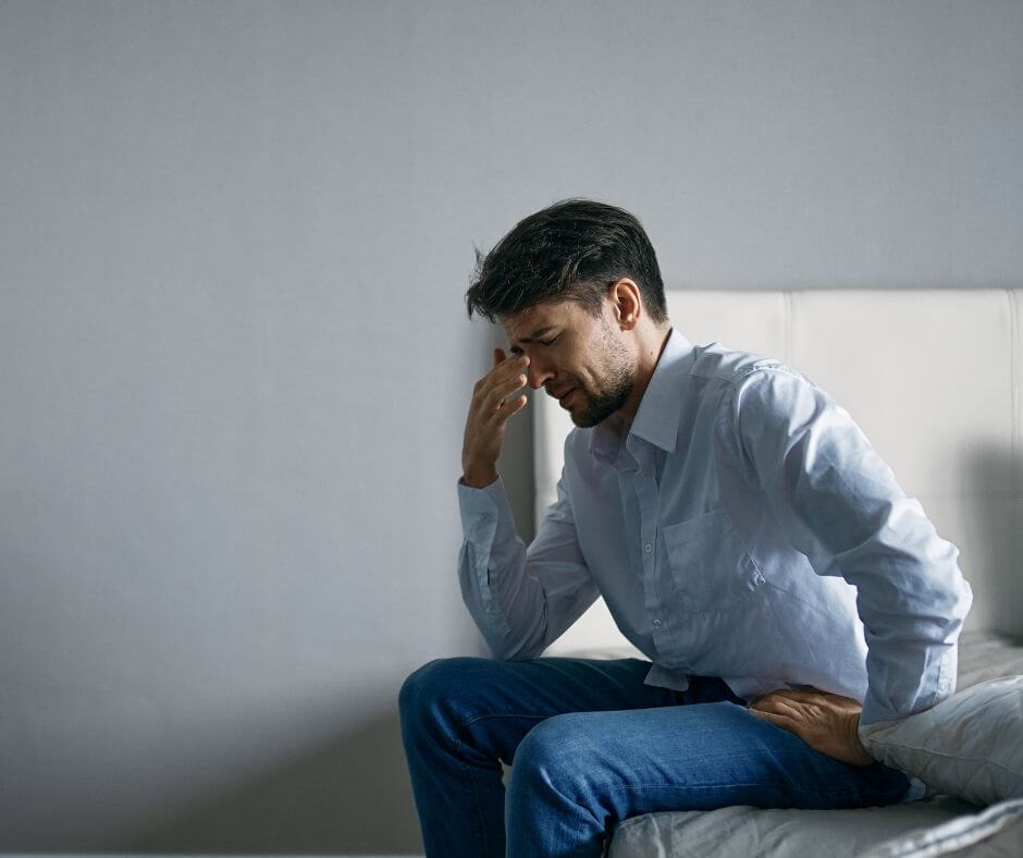 Man sits on the edge of a bed with a remorseful look on his face