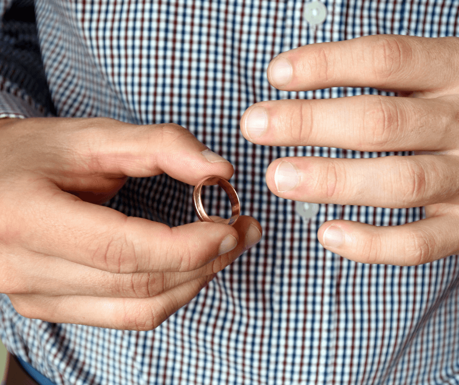 A person with light skin and more masculine hands either removes or replaces a gold wedding band.