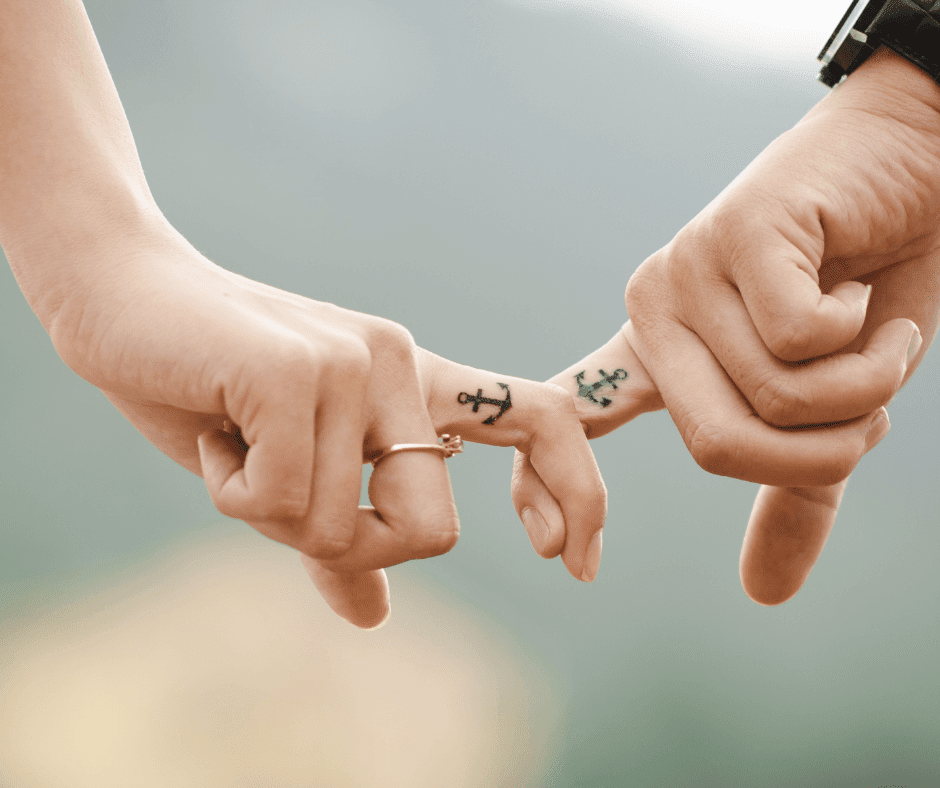 Photo shows two white hands interlinking index fingers only with anchor tattoos on the fingers