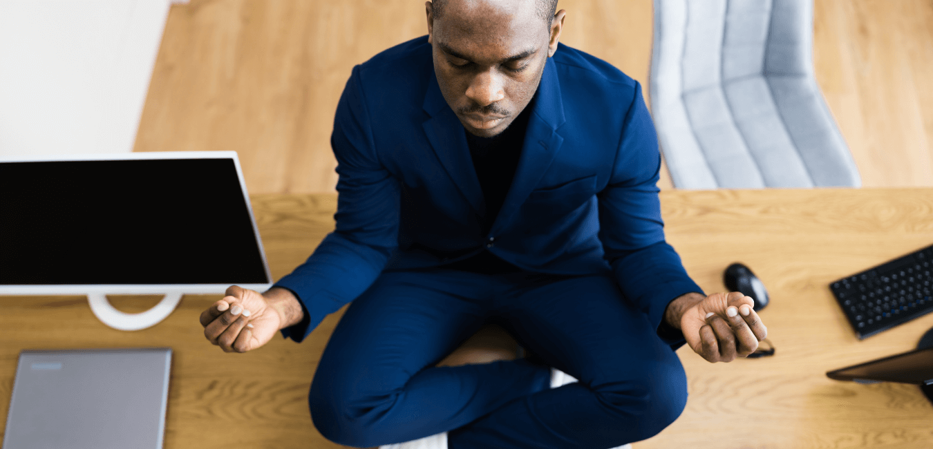 A black male sits on the floor next to his computer in a meditation stance