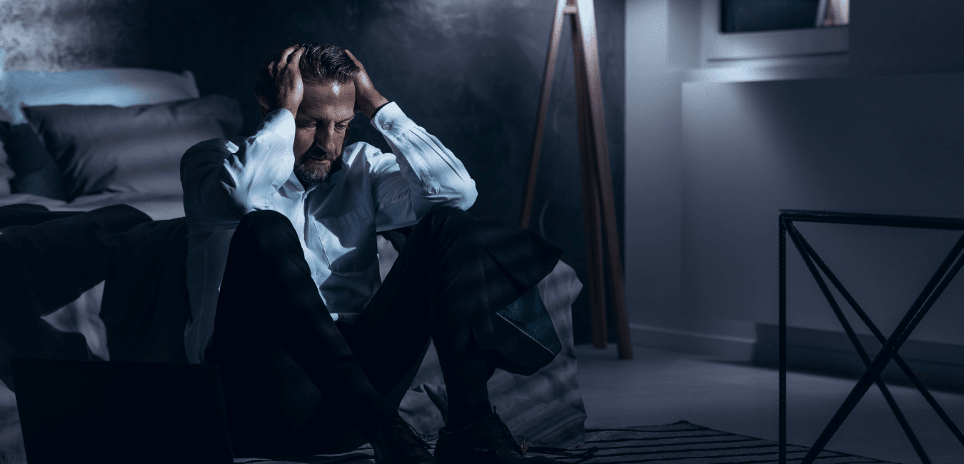 Man wearing office attire on his bed looking problematic in a dark room