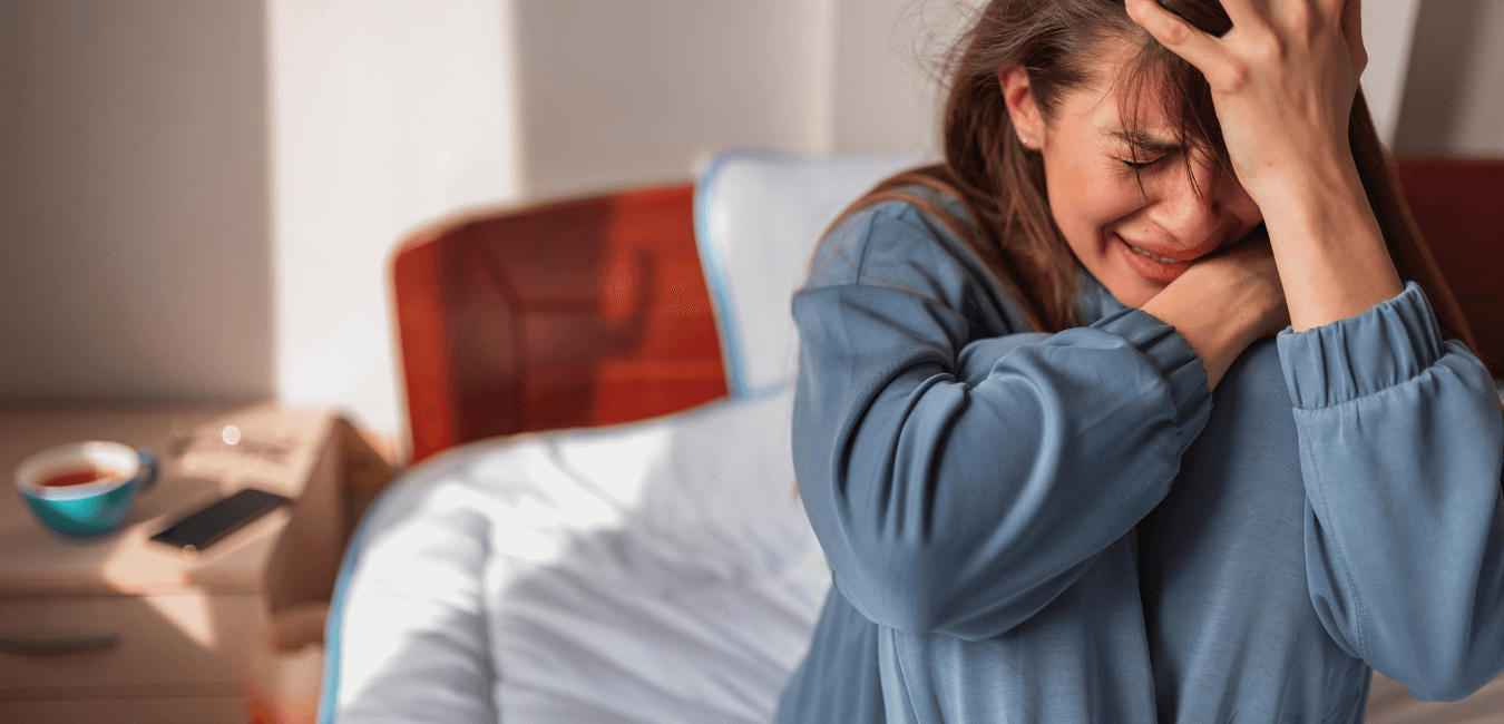 Woman wearing sleep ware sitting on her bed sobbing