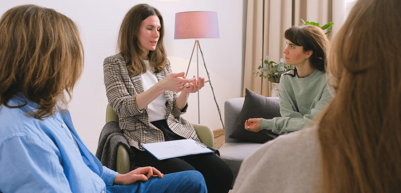Woman speaking and sharing experiences during a group session, with all other women listening in a room