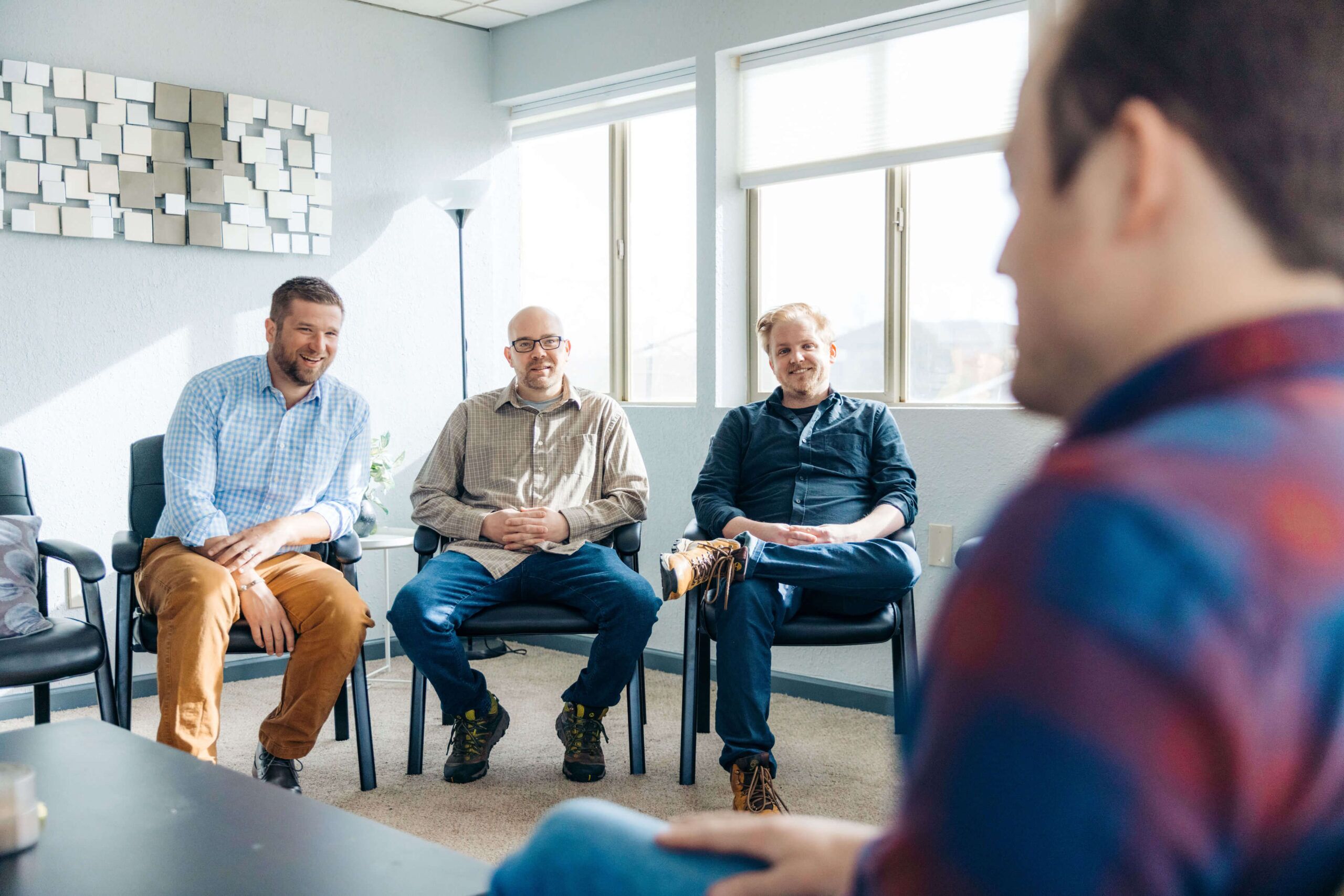A man sits in a circle during all-men group therapy, speaking while the others listen
