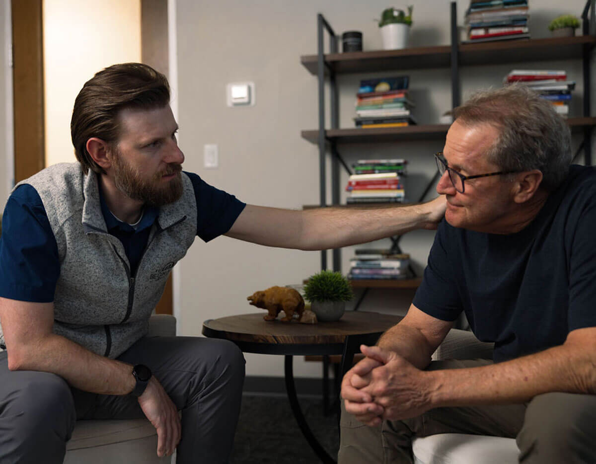 A therapist offering support by placing a reassuring hand on a client’s shoulder during a one-on-one session, reflecting empathy, trust, and compassionate guidance.