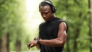 Man of color outdoors in headphones, looking at his smartwatch before running.