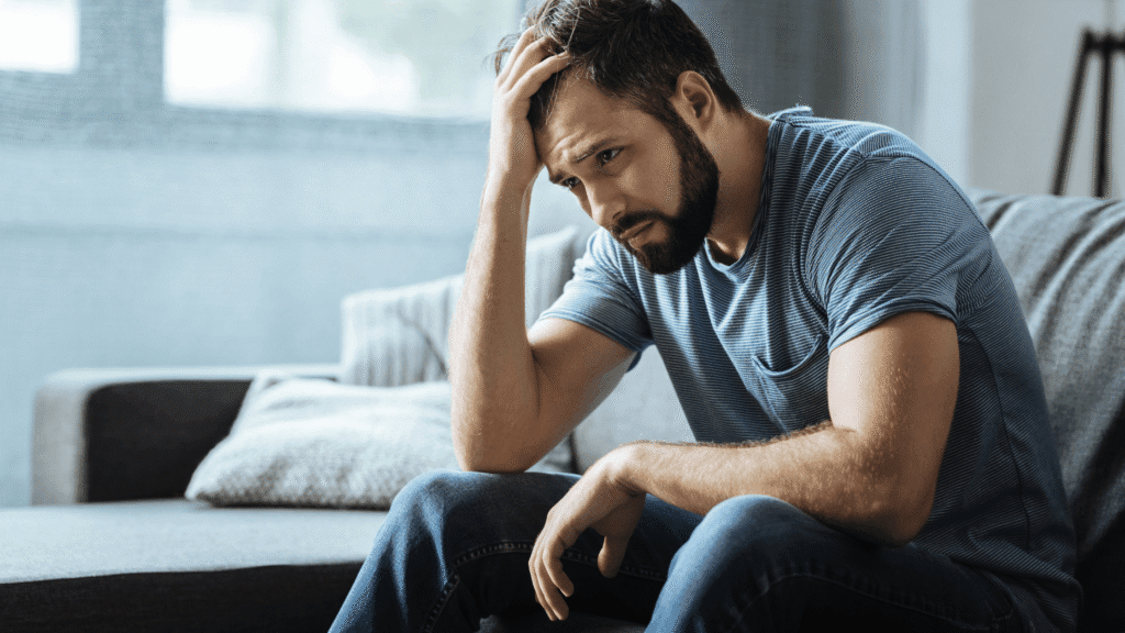 Man sitting in living room with his hand on his head, appearing deep in thought.