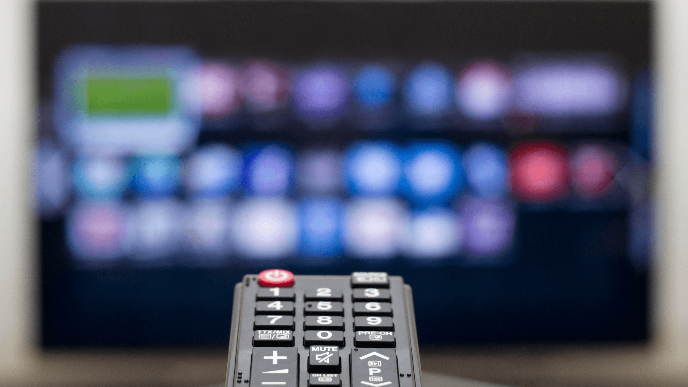 Close-up of a hand holding a remote pointed at a TV screen