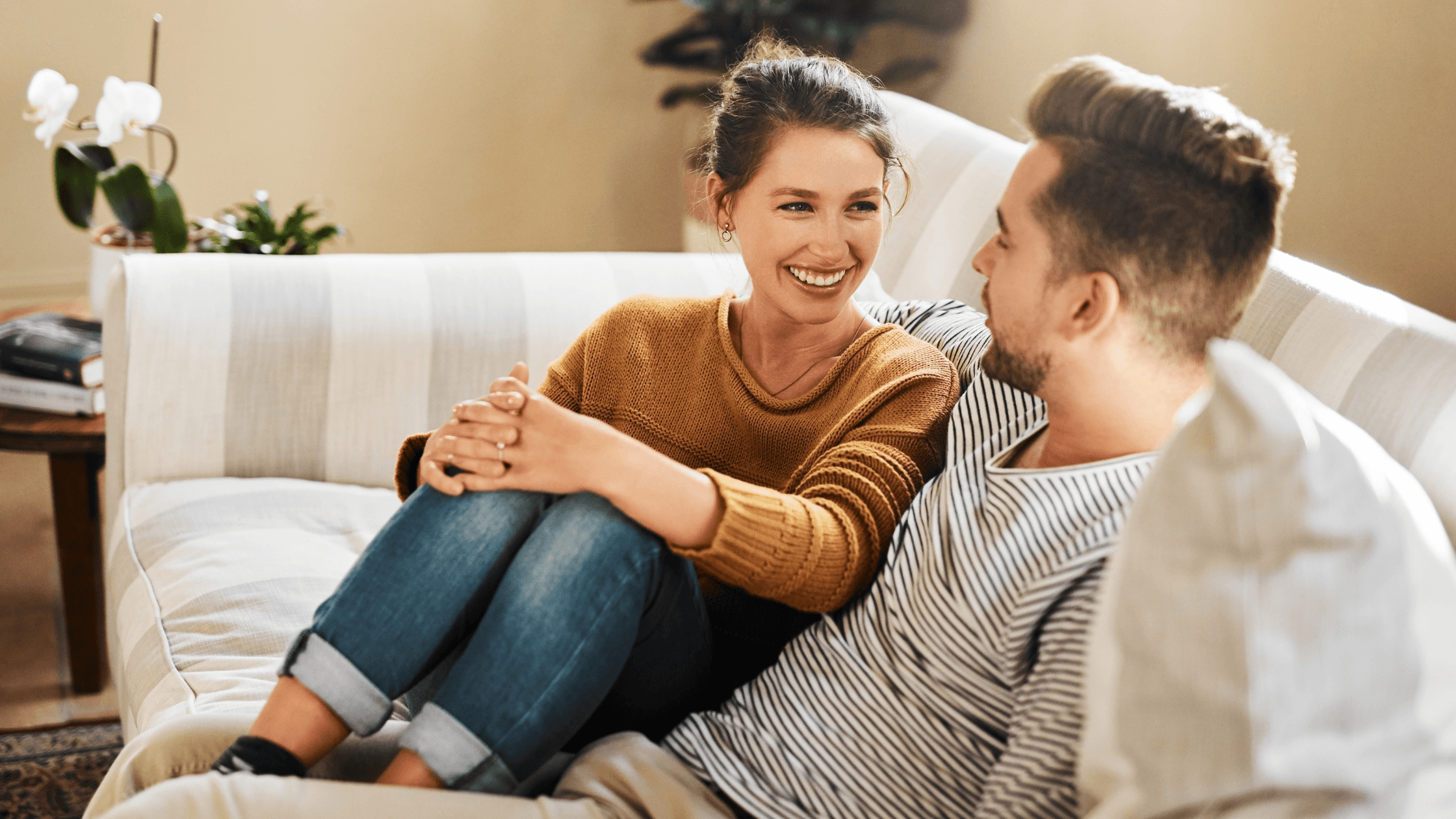 Couple sitting together on a couch at home, looking happy and secure in their relationship.