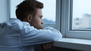 Man looking out window quietly, appearing deep in thought
