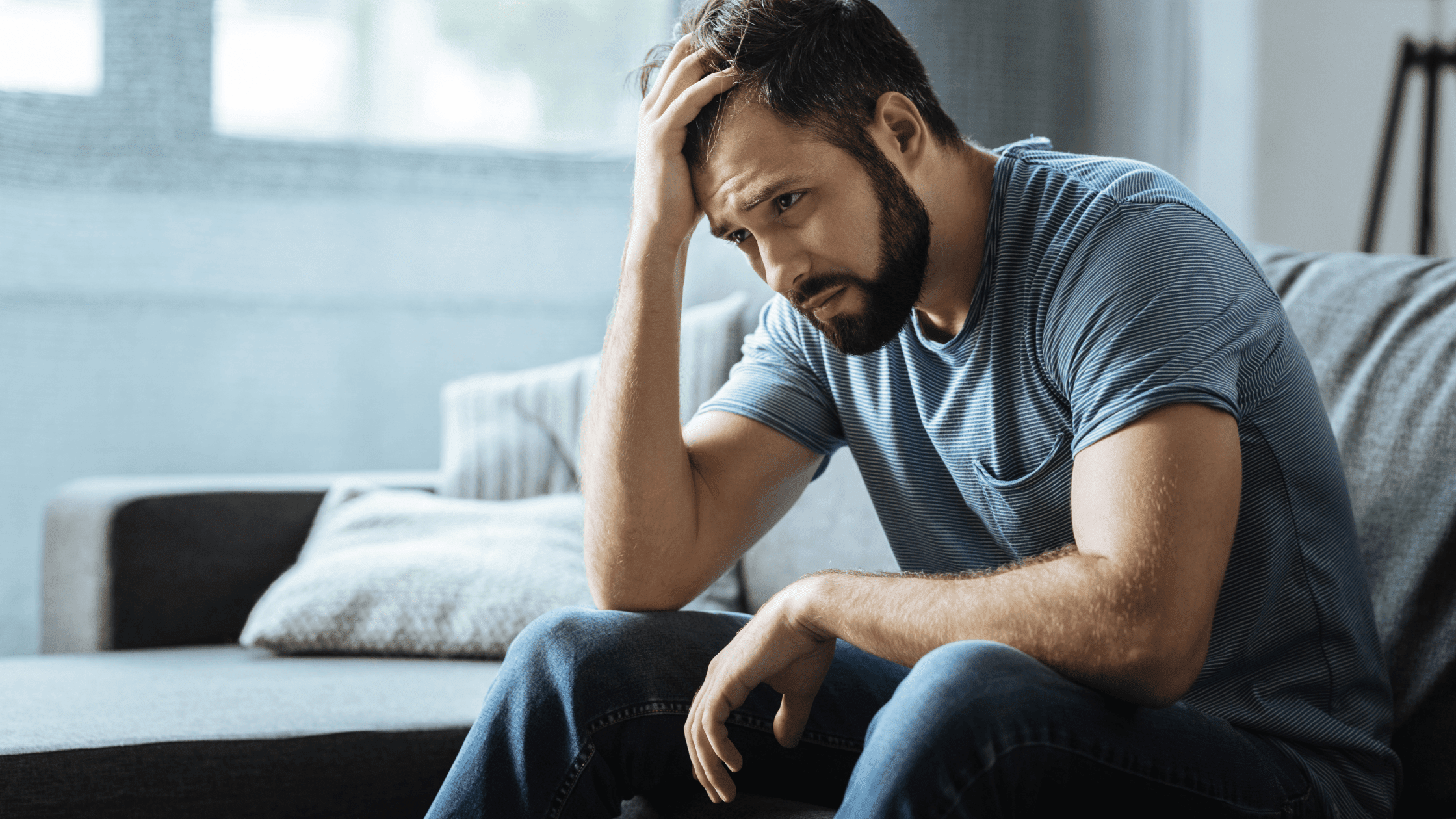 Man sitting in living room with his hand on his head, appearing deep in thought.