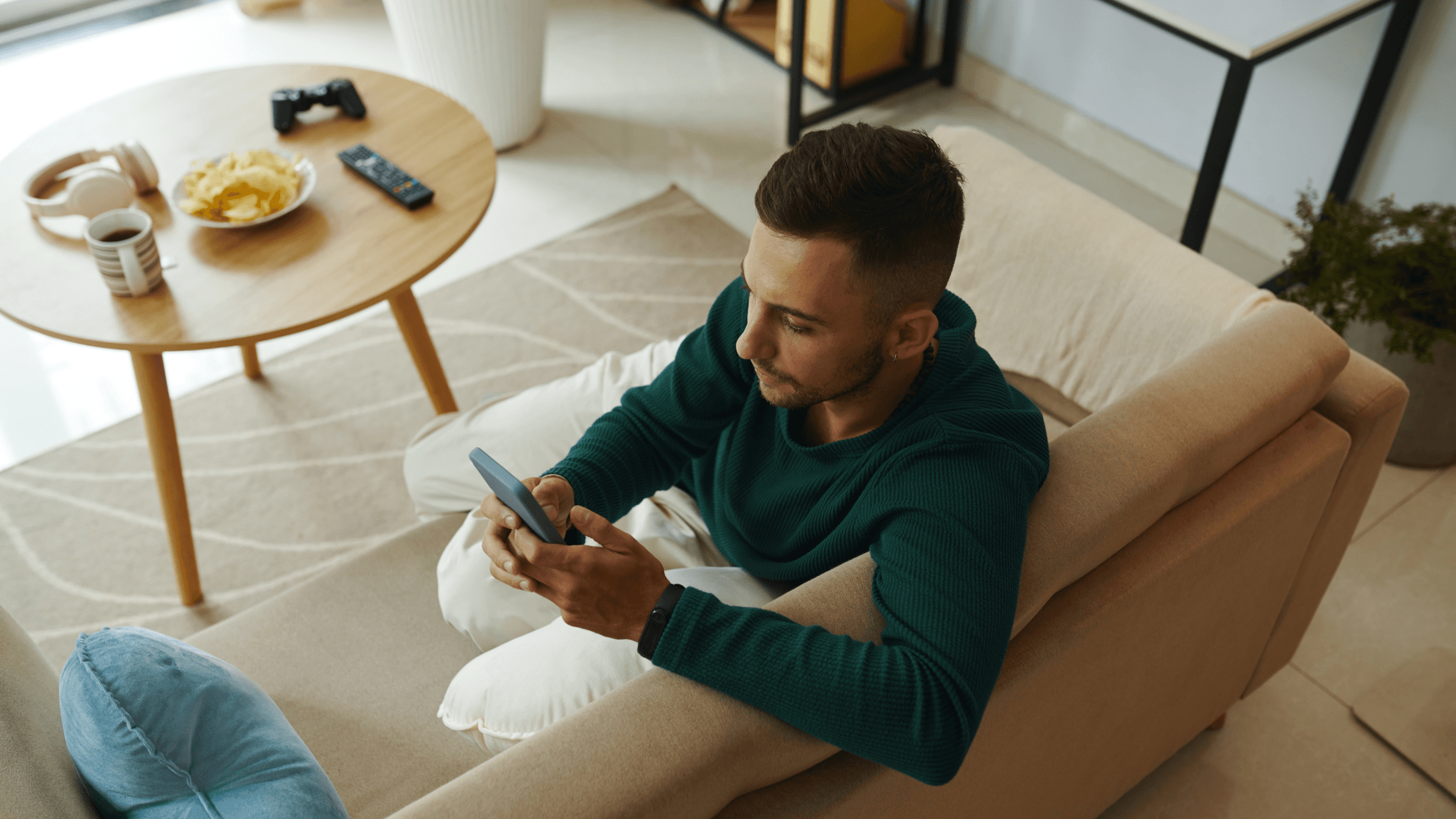 Man sitting comfortably on a sofa at home, focused on his phone, with a calm and relaxed posture.