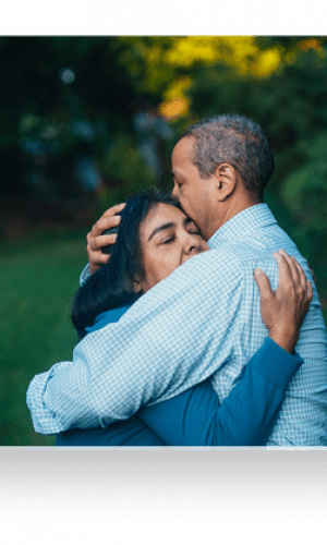 A man and woman embrace in a very green field.