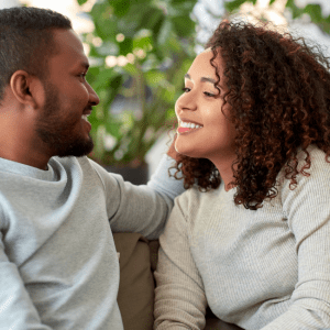 Two people, a man and a woman look at each other with smiles while sitting on a couch