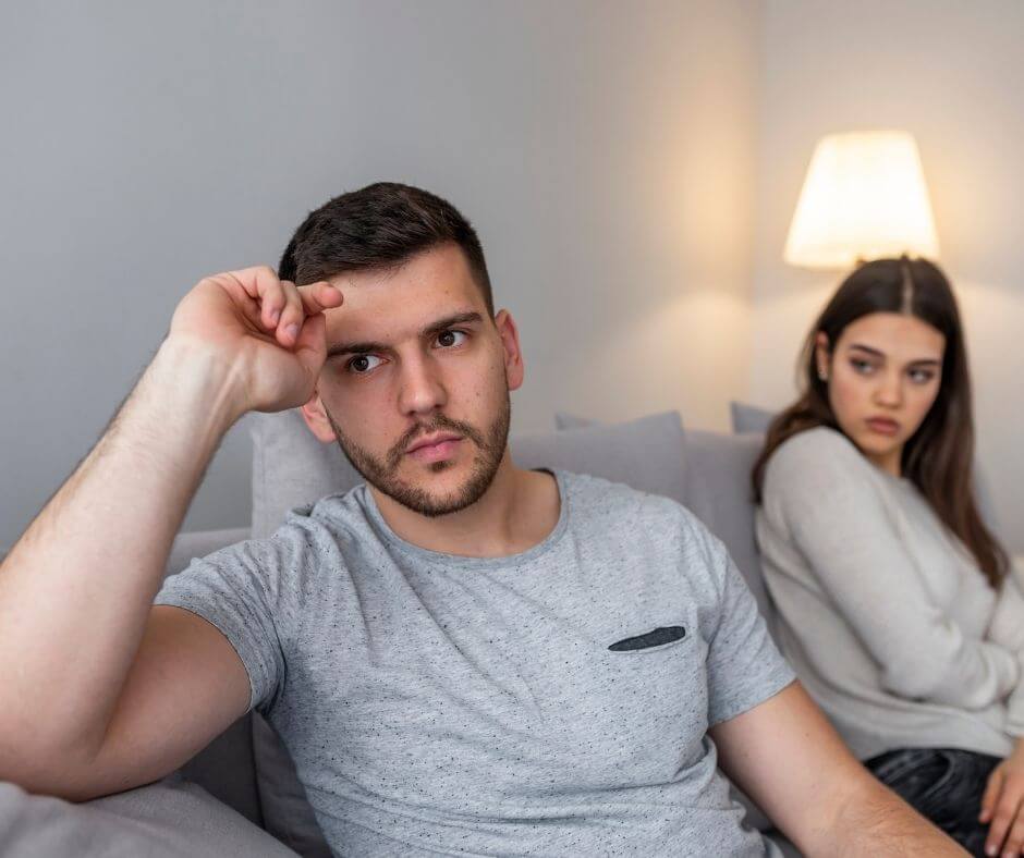 Couple sitting on a couch. The man has his back turned on the woman