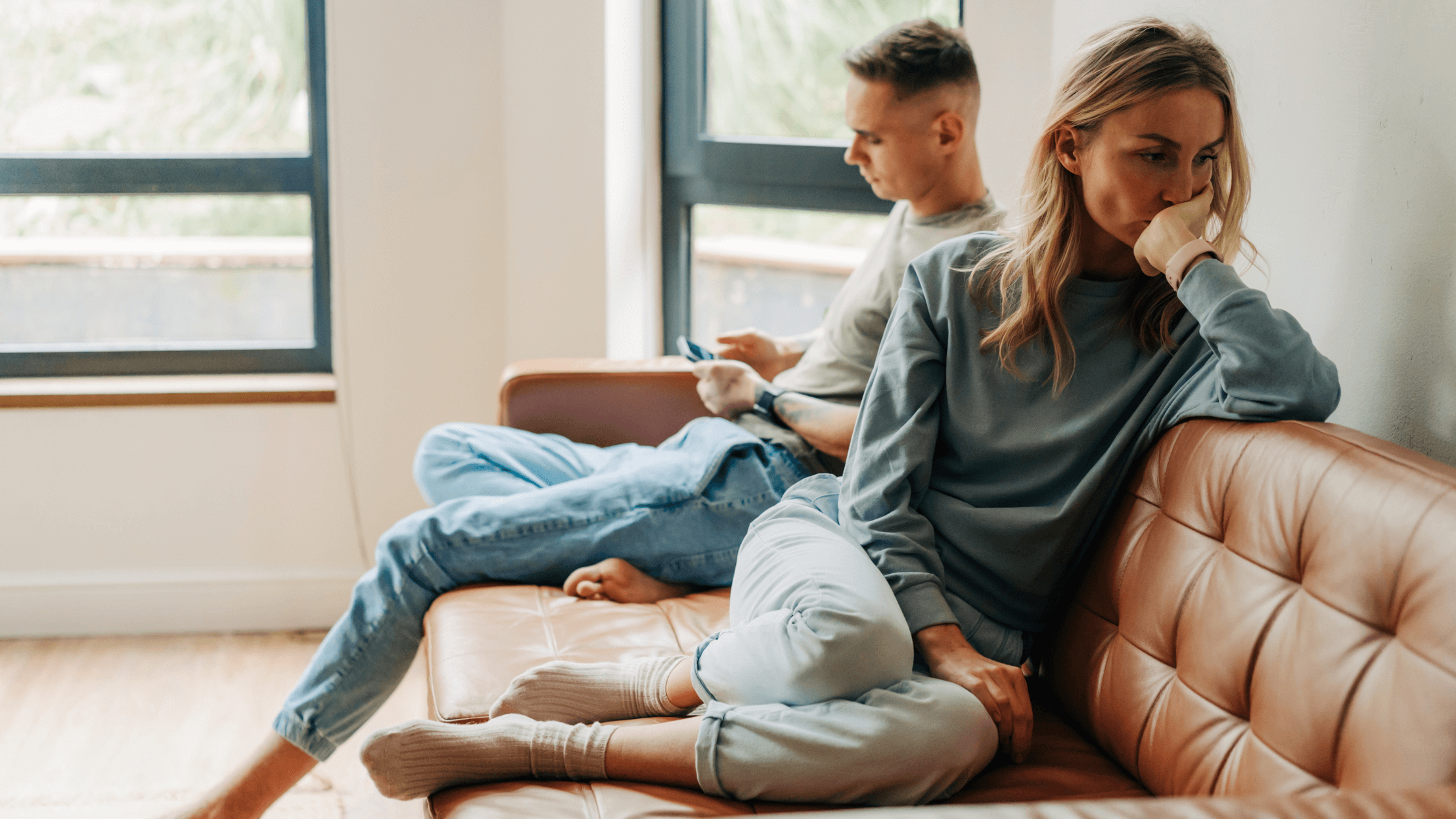 Couple sits quietly on the couch at home, not looking at each other, seeming to have a problem.
