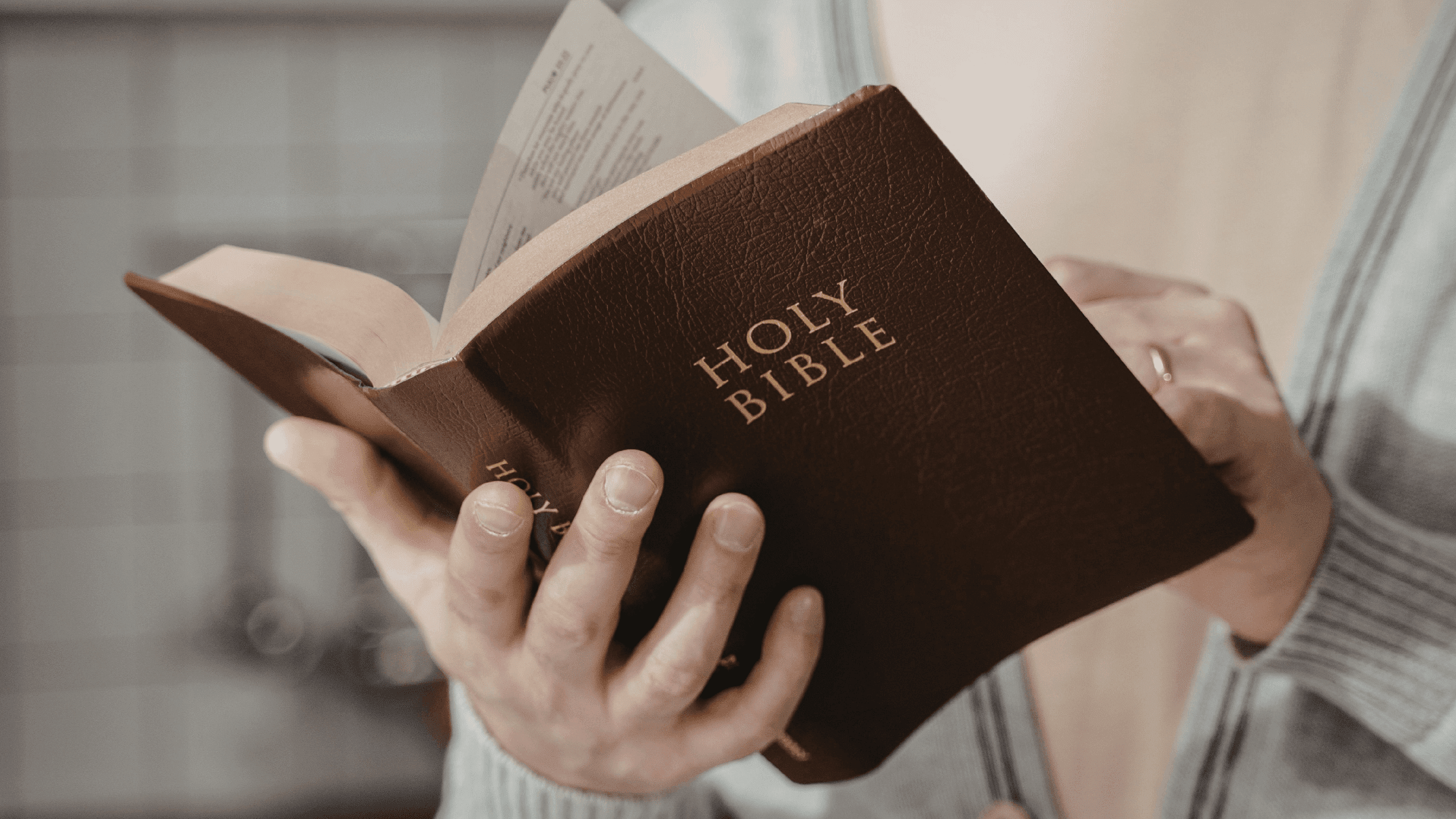 Close-up of a married person wearing a wedding ring, holding and reading a holy Bible.