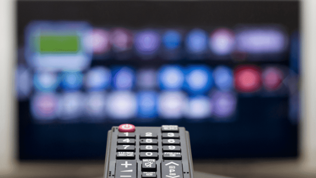 Close-up of a hand holding a remote pointed at a TV screen