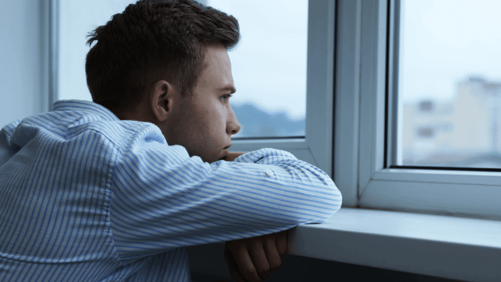 Man looking out window quietly, appearing deep in thought