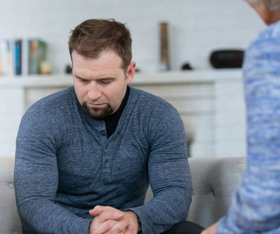 A man sitting on a couch looking sad and worried.