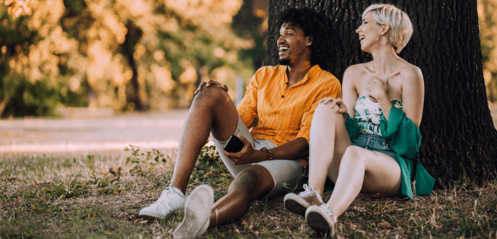 Young couple sitting at the park behind the tree talking and having fun