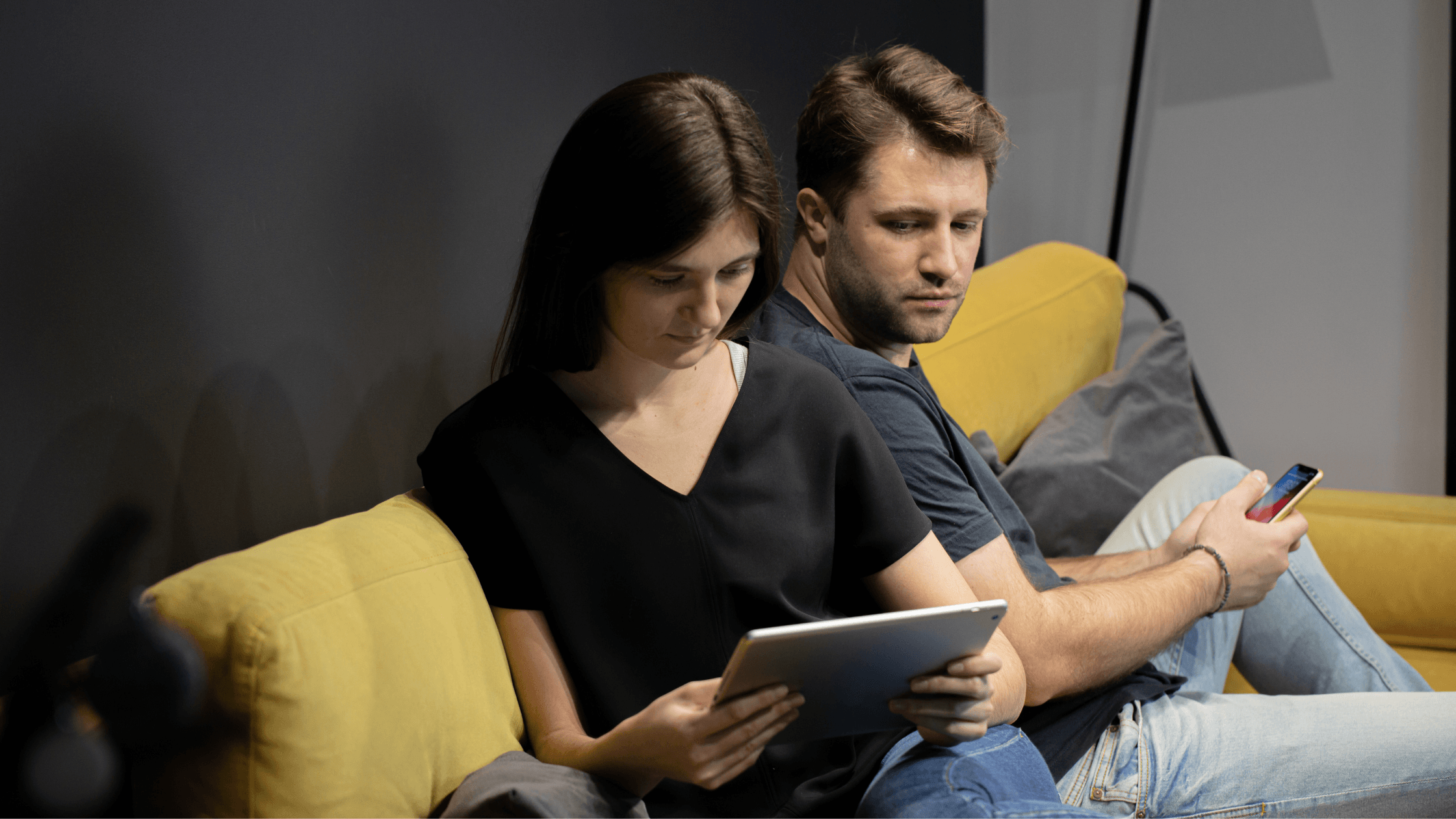 Couple sitting at home. Woman busy with her iPad. Man looks at her, seeming left out.
