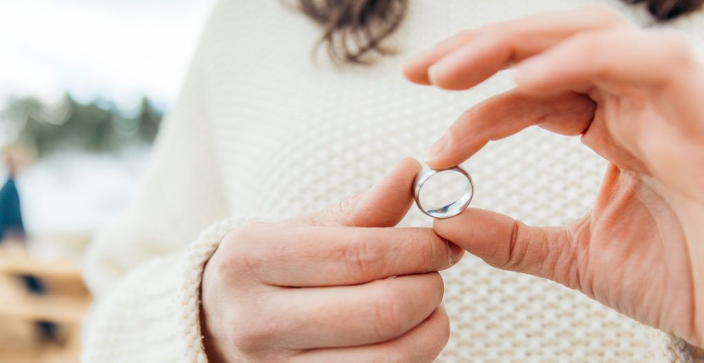 A woman holds her wedding ring between her fingers. Only her hands are visible in the photo