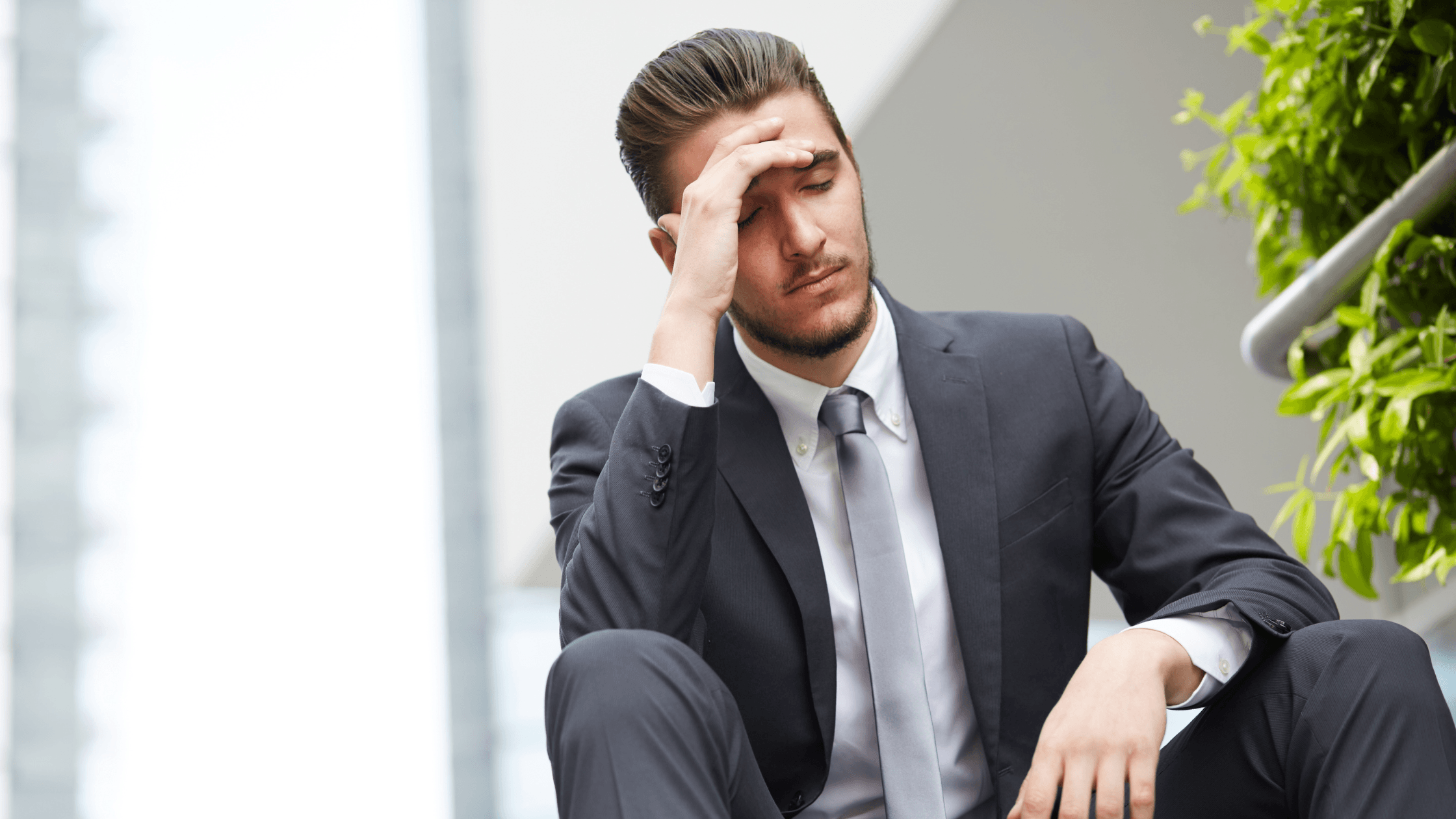Man in tuxedo sitting outside with his hand on his forehead, looking worried.